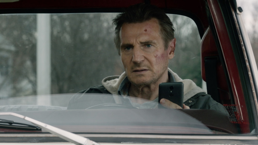 Resni Liam Neeson v avtomobilu z mobitelom v roki.